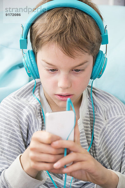Portrait des Jungen mit Smartphone und Kopfhörer auf Sitzsack liegend