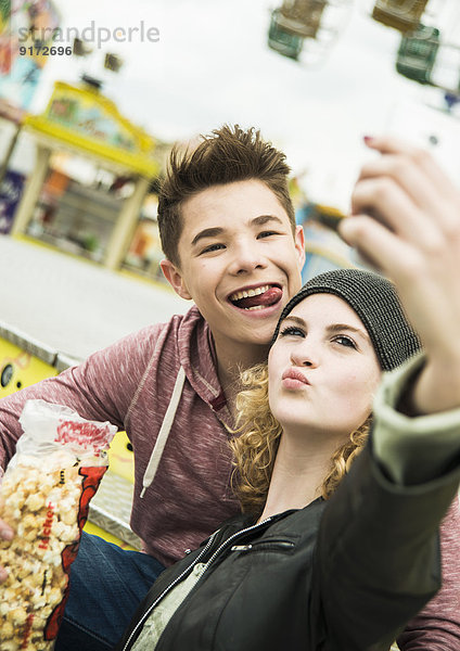Porträt eines Teenagerpaares mit Popcorn  das sich auf dem Jahrmarkt fotografiert.