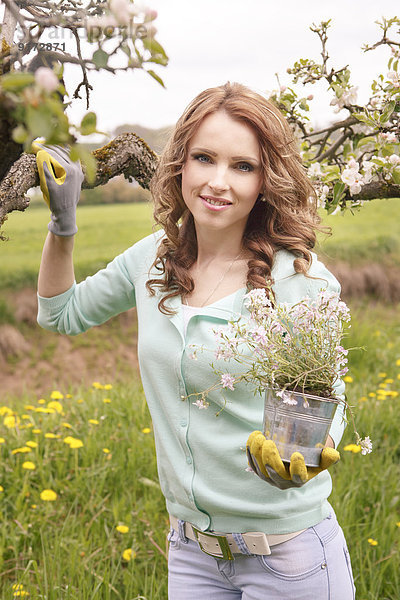 Porträt der lächelnden Frau mit Blumentopf im Garten