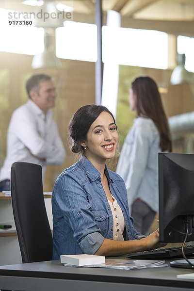 Portrait der Geschäftsfrau am Schreibtisch mit kommunizierenden Kollegen im Hintergrund