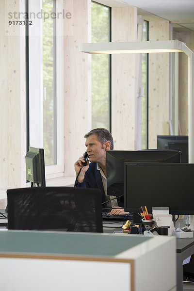 Porträt eines Geschäftsmannes beim Telefonieren am Arbeitsplatz