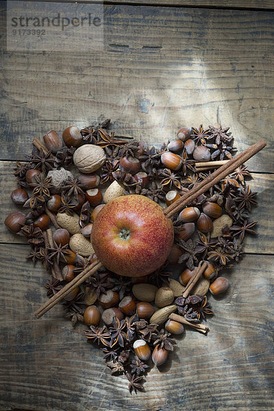 Herz in Form von Sternanis  Nüssen und Zimtstangen mit Apfel  durchbohrt von Zimtstangen auf Holz