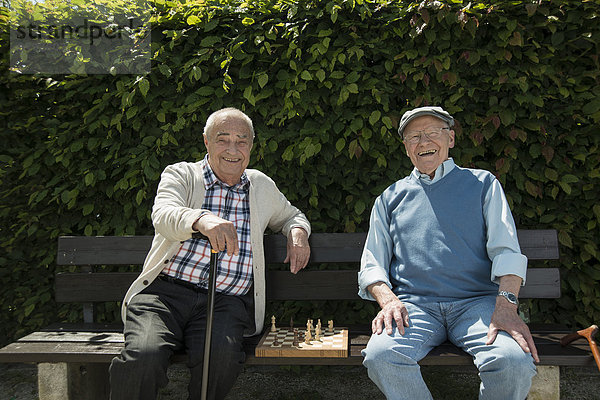 Zwei alte Freunde sitzen auf einer Parkbank mit Schachspiel