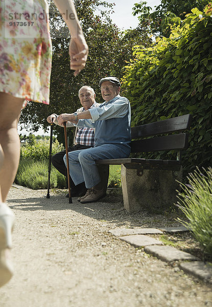 Zwei alte Männer sitzen auf der Parkbank und beobachten die Beine der vorbeifahrenden Frau.