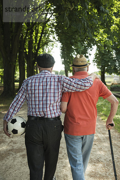 Zwei alte Freunde beim Spaziergang im Park mit Fußball  Rückansicht