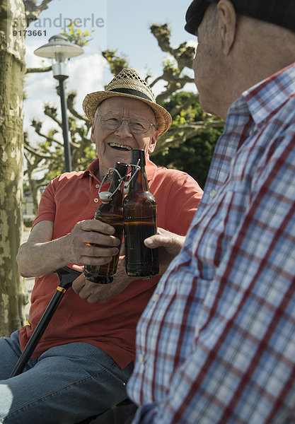 Zwei alte Freunde stoßen mit Bierflaschen im Park an.