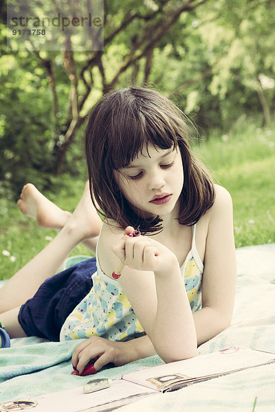 Porträt eines kleinen Mädchens  das auf einer Decke im Garten liegt und ein Tagebuch schreibt.