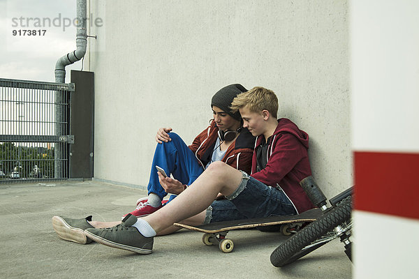 Zwei Jungen sitzen auf dem Boden und schauen auf das Handy.