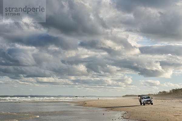 Australia  New South Wales  Pottsville  off-road vehicle standing on beach with surf and dark clouds