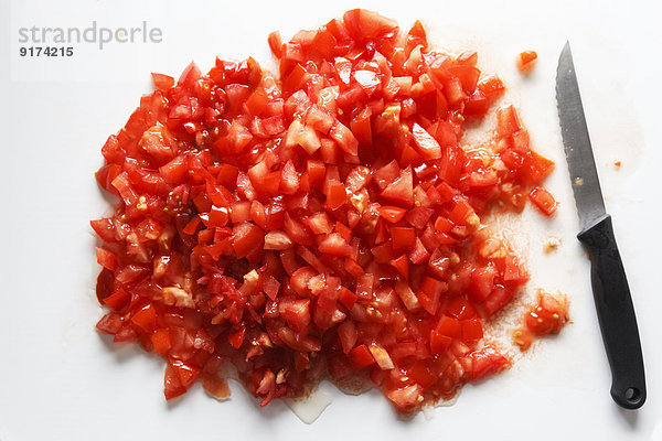 Diced tomatoes and kitchen knife on white ground