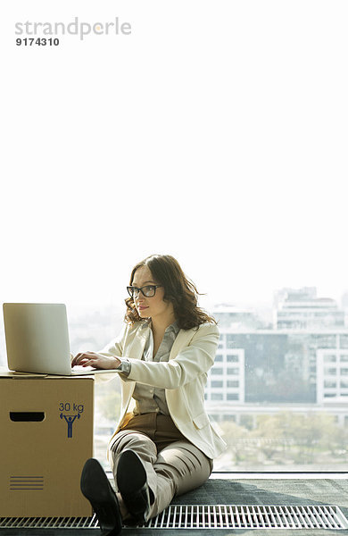 Geschäftsfrau mit Laptop auf leerer Büroetage mit Pappkartons