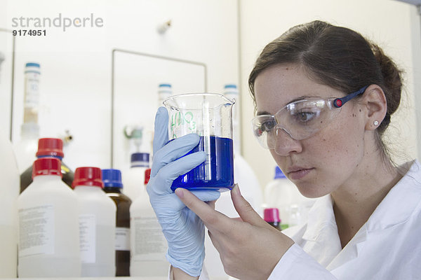 Portrait einer jungen Chemikerin mit Becher mit blauer Flüssigkeit