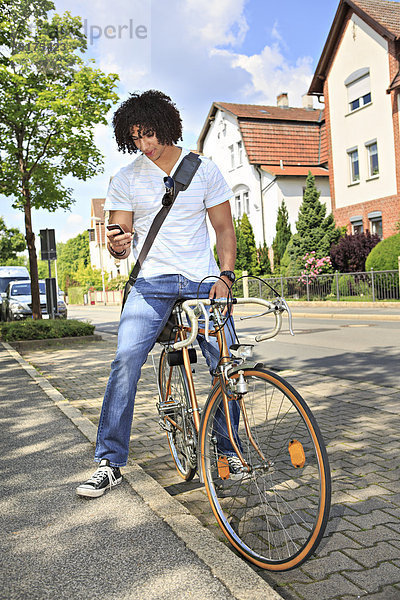 Ein junger Student sitzt auf einem Fahrrad und schaut auf sein Smartphone.
