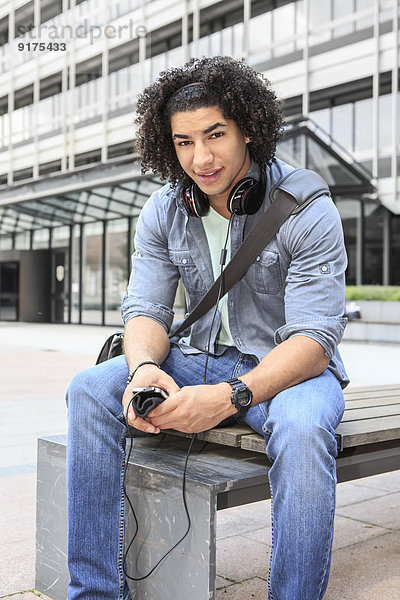 Junger Student auf der Bank sitzend mit seinem Smartphone