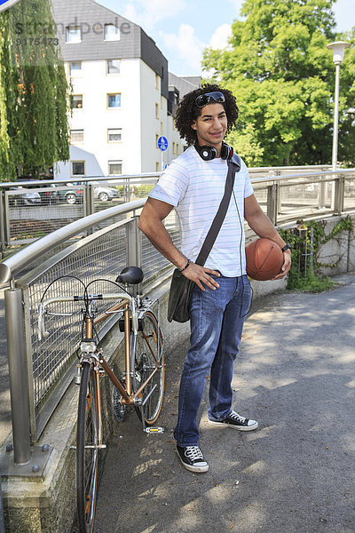 Junger männlicher Schüler mit Basketball neben seinem Rennrad