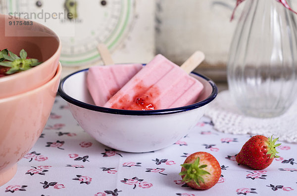 Schale mit zwei Erdbeereis-Lollies und Erdbeeren auf Tuch