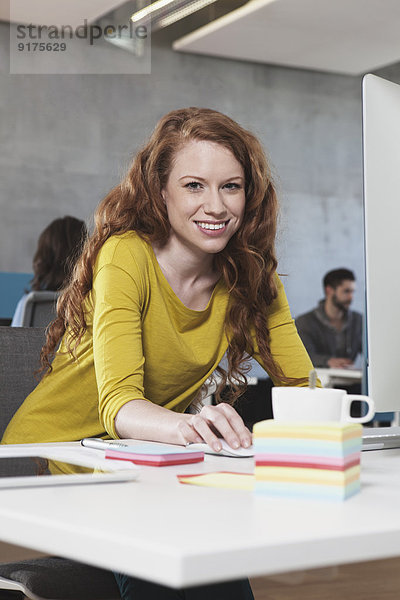 Porträt einer lächelnden Frau an ihrem Arbeitsplatz im Großraumbüro