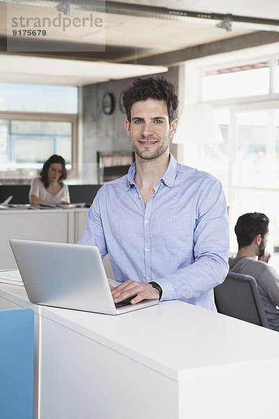 Porträt eines lächelnden Mannes mit Laptop im Open Space Office