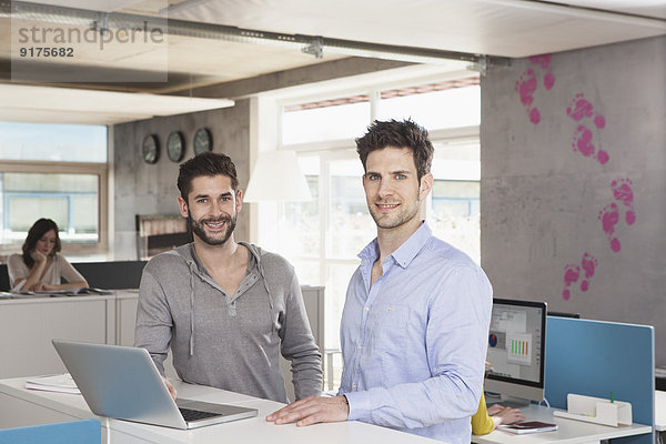 Portrait von zwei Kollegen mit Laptop in einem Großraumbüro
