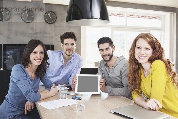 Gruppenbild von vier kreativen Menschen  die einen Tablet-Computer im Büro zeigen.