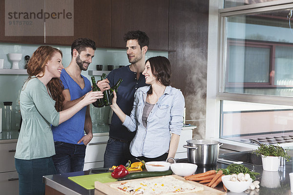 Porträt von vier Freunden  die mit Bierflaschen in der Küche anstoßen.