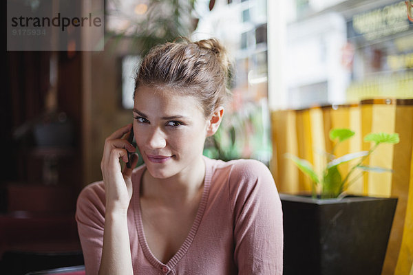 Frankreich  Paris  Porträt einer jungen Frau  die mit ihrem Smartphone in einem Café telefoniert.