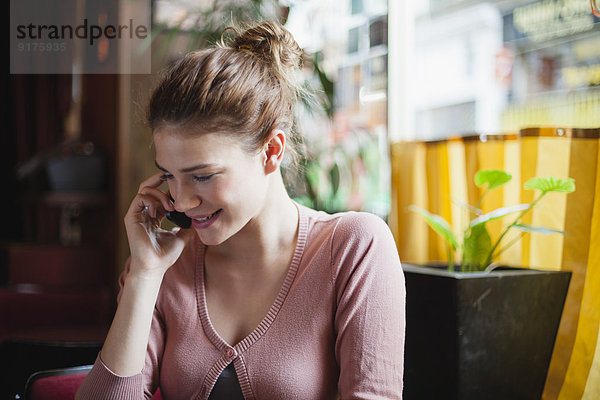 Frankreich  Paris  Porträt einer jungen Frau  die mit ihrem Smartphone in einem Café telefoniert.