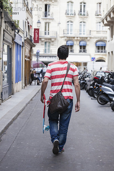 Frankreich  Paris  Mann mit Skateboard  der auf einer Straße läuft.