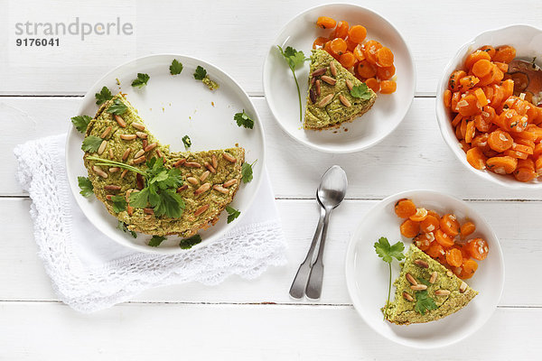 Teller gebackene Erbsenkuchen mit Pinienkernen  garniert mit glatter Petersilie und Schale mit gedämpften Karotten