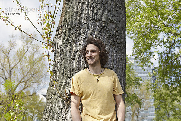 Lächelnder junger Mann am Baumstamm
