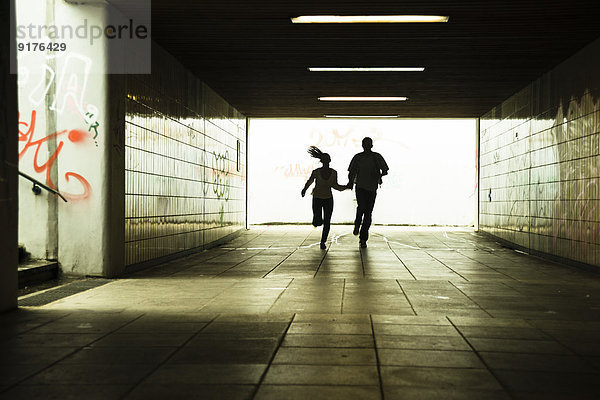 Junges Paar läuft zusammen in einer dunklen Unterführung