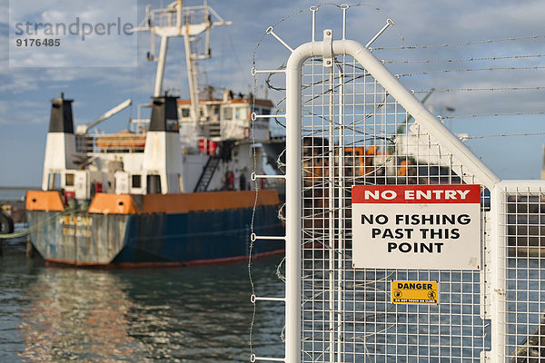 Neuseeland  Nelson  Zaun ohne Einfahrtsschild und ein Schiff im Hafen