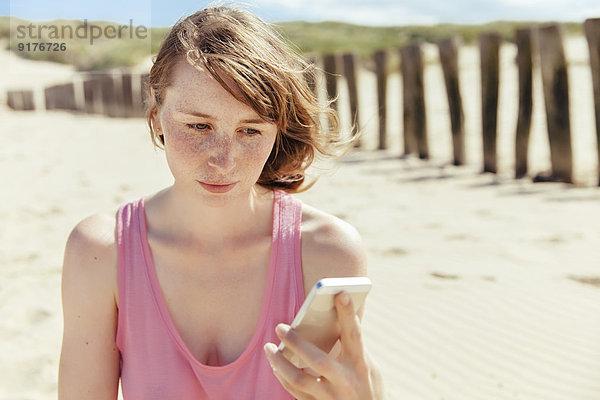Frau schaut auf ihr Smartphone am Strand