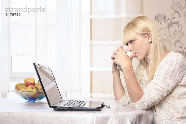 Porträt einer jungen Frau mit Tasse am Laptop zu Hause