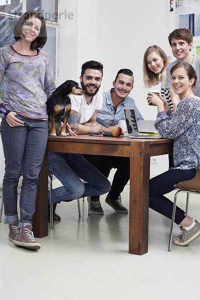Gruppe von Kreativprofis mit Hund am Tisch