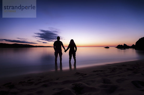 Spanien  Menorca  Paar beobachtet Sonnenuntergang am Playa de Cavalleria
