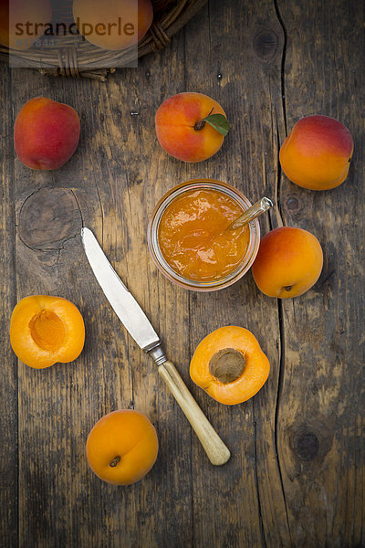 Glas Aprikosenmarmelade  Messer und geschnittene und ganze Aprikosen auf Holz  erhöhte Ansicht