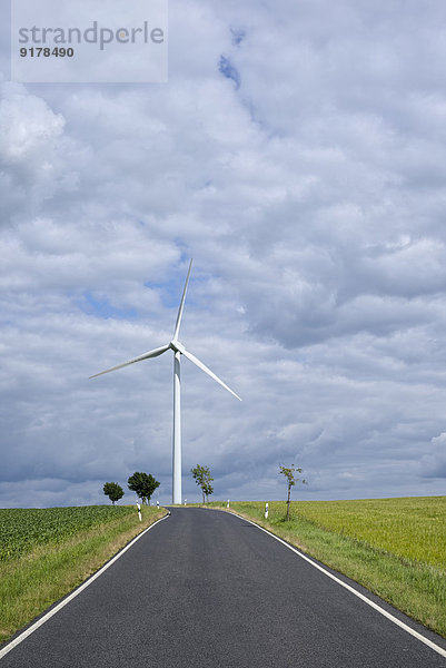 Deutschland  Sachsen  Leere Straße und Windkraftanlage