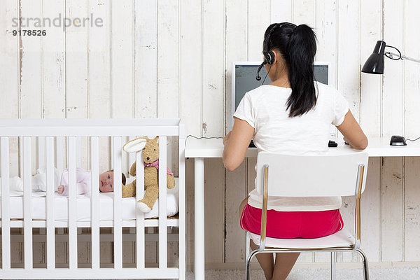 Frau arbeitet im Home Office  während ihr Baby im Kinderbett liegt.