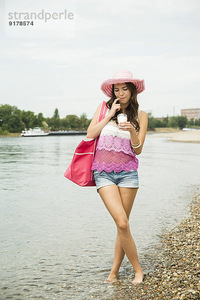 Junge Frau mit Hut und Tasche am Rheinufer stehend