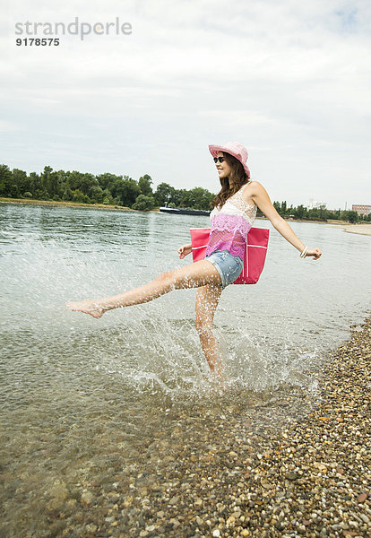 Junge Frau mit Hut und Tasche hat Spaß am Rheinufer