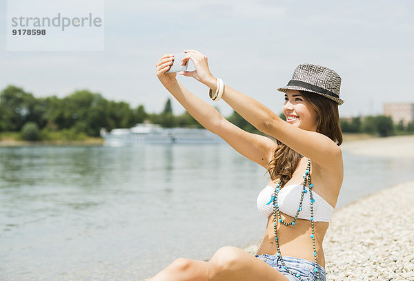 Porträt einer jungen Frau  die einen Selfie mit ihrem Smartphone am Strand nimmt.