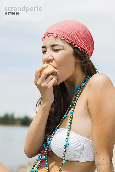 Porträt einer jungen Frau beim Essen eines Apfels am Strand