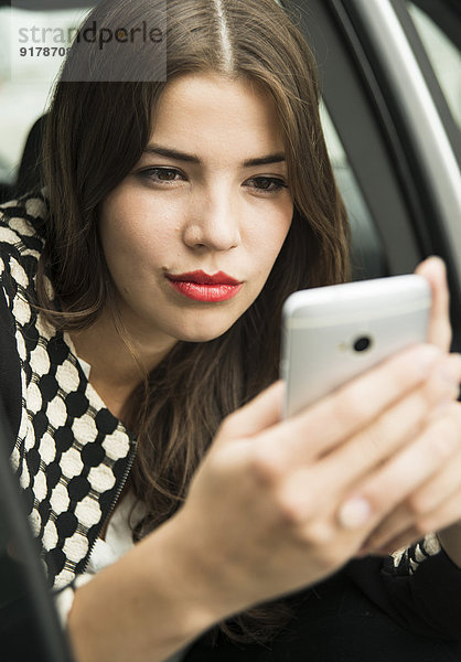 Porträt einer jungen Frau  die im Auto sitzt und einen Selfie mit ihrem Smartphone nimmt.