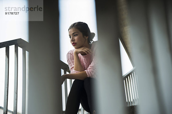 Junge Frau  die auf einer Treppe sitzt und etwas beobachtet.