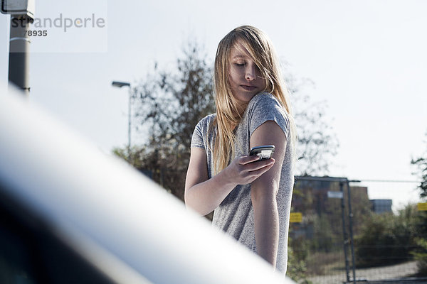 Blonde junge Frau mit Handy im Freien