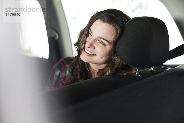 Lächelnde junge Frau auf dem Rücksitz eines Autos