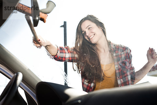 Lächelnde junge Frau reinigt Windschutzscheibe eines Autos