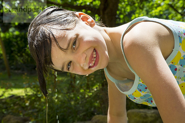 Porträt eines lachenden kleinen Mädchens mit tropfnassem Haar im Garten