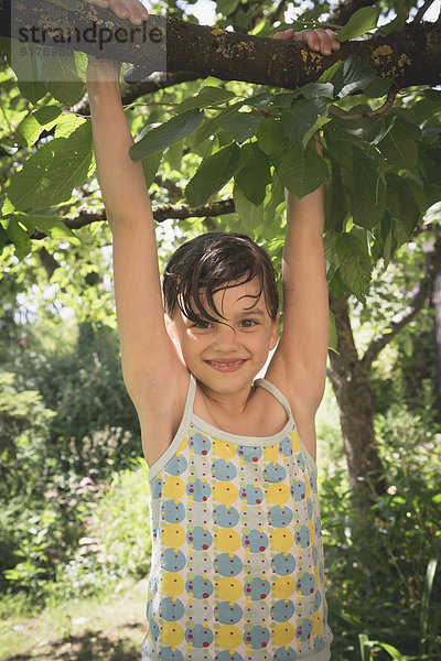 Porträt eines lächelnden kleinen Mädchens  das auf einen Baum klettert.